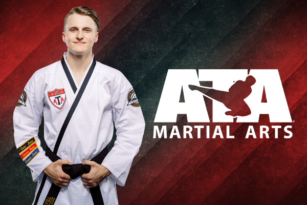 Martial arts instructor in a white ATA uniform standing confidently with arms crossed in front of an ATA Martial Arts logo.
