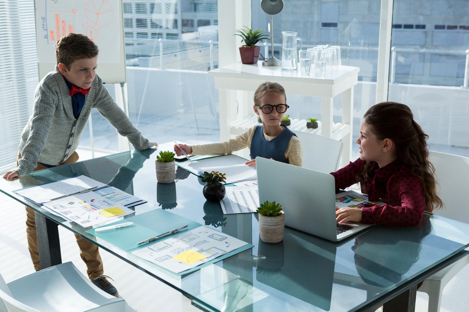 Children sitting at a conference-style table in a bright modern room, practicing leadership and communication skills as part of the Mini CEOs™ program.